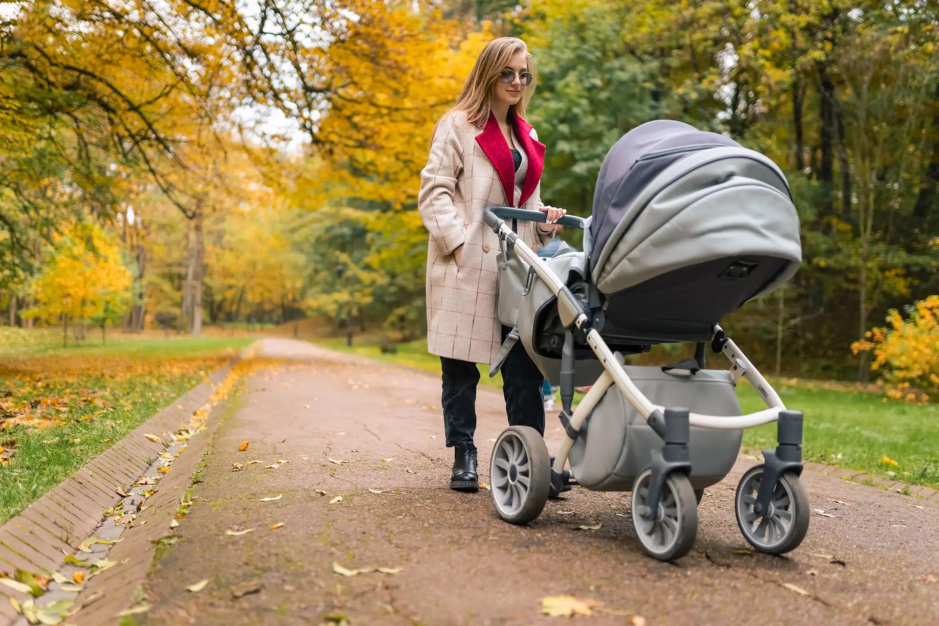 Woman walking in a park with a modern baby stroller on an autumn day.